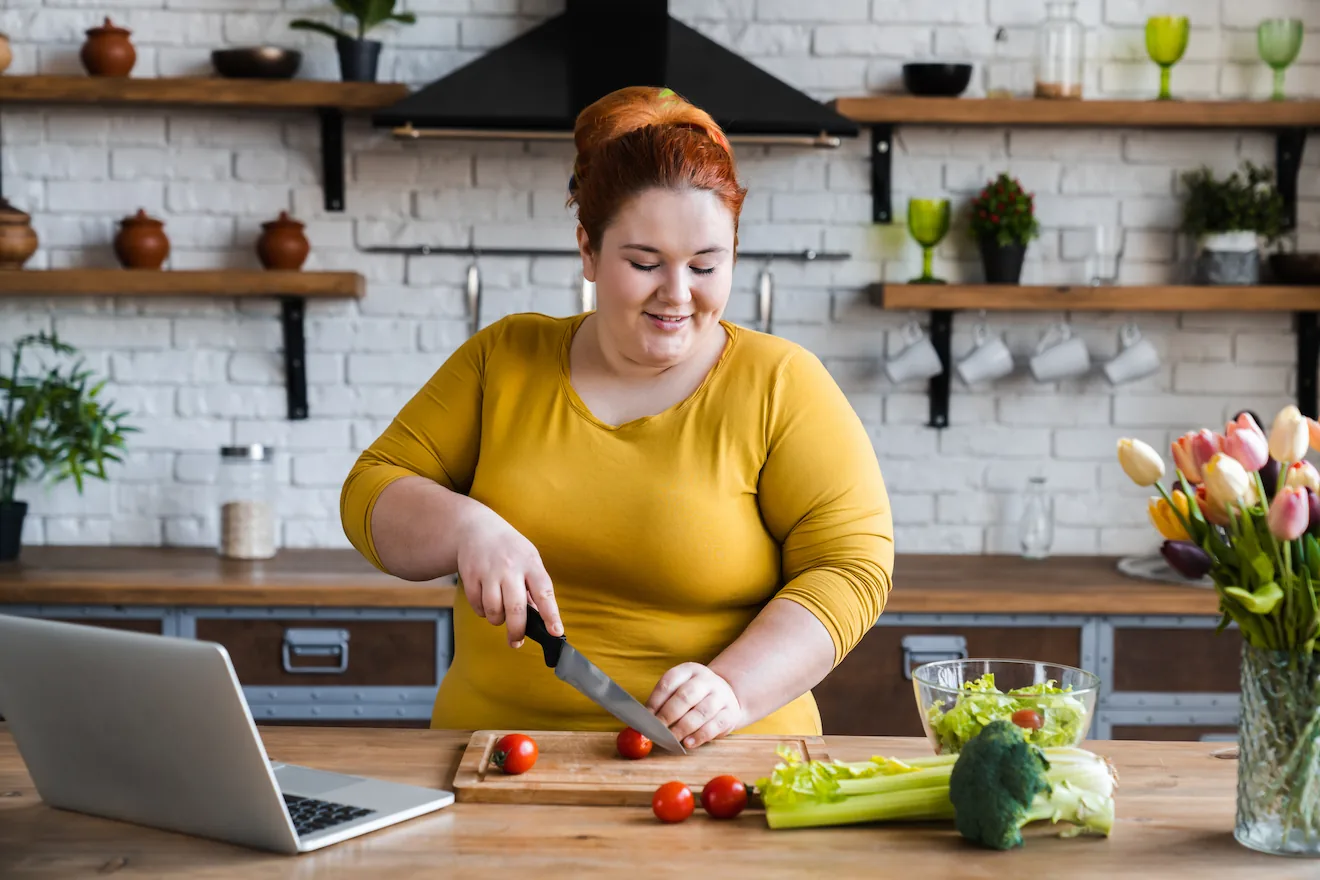 Overweight woman cutting vegetables in the kitchen