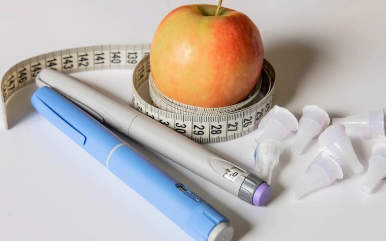 Injections pens laying beside measuring tape and apple